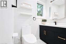 Bathroom featuring a white toilet, black vanity with gold-tone hardware, white countertop, and a single window - 