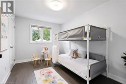 Light-filled room featuring dark wood-finish flooring, white walls, and a prominent window with a roller shade - 