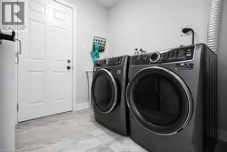 Dedicated laundry area featuring a front-loading washer and dryer set, light gray wall paint, and light-toned tile flooring - 