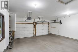 Two-car garage featuring automatic garage door openers, concrete flooring, overhead lighting, a side window with dark trim, and built-in white cabinetry - 
