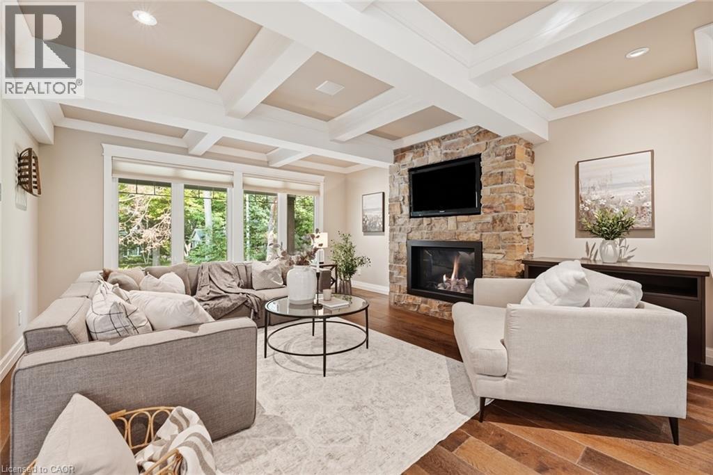 Living area featuring a stone-clad fireplace with built-in media integration, large windows, wood-finish flooring, recessed lighting, and a coffered ceiling - 266 Ferndale Place, Waterloo, ON - Indoor Photo Showing Living Room With Fireplace
