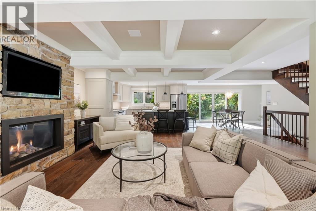 Spacious living area featuring a stone fireplace with a mounted television, wood-finish flooring, a coffered ceiling, and an open-concept layout to the kitchen and dining areas - 266 Ferndale Place, Waterloo, ON - Indoor Photo Showing Living Room With Fireplace
