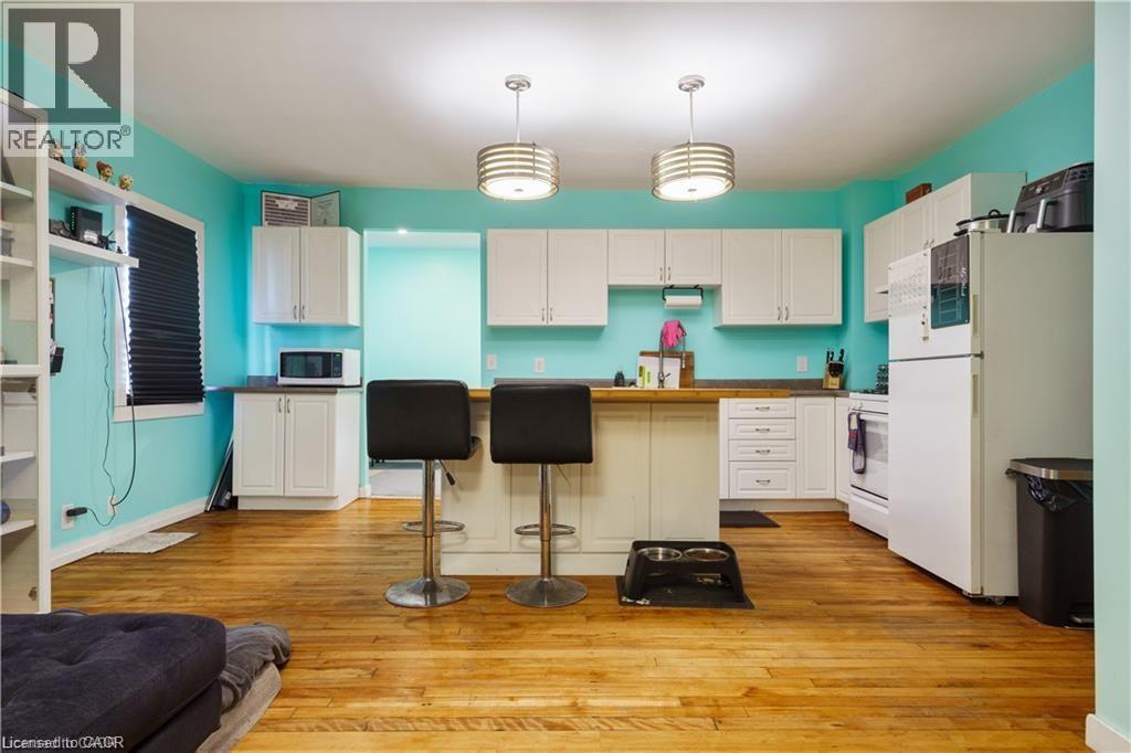 Open concept kitchen featuring light wood floors, white cabinetry, a kitchen island with seating, and a white refrigerator - 219 Avondale Street, Hamilton, ON - Indoor Photo Showing Kitchen
