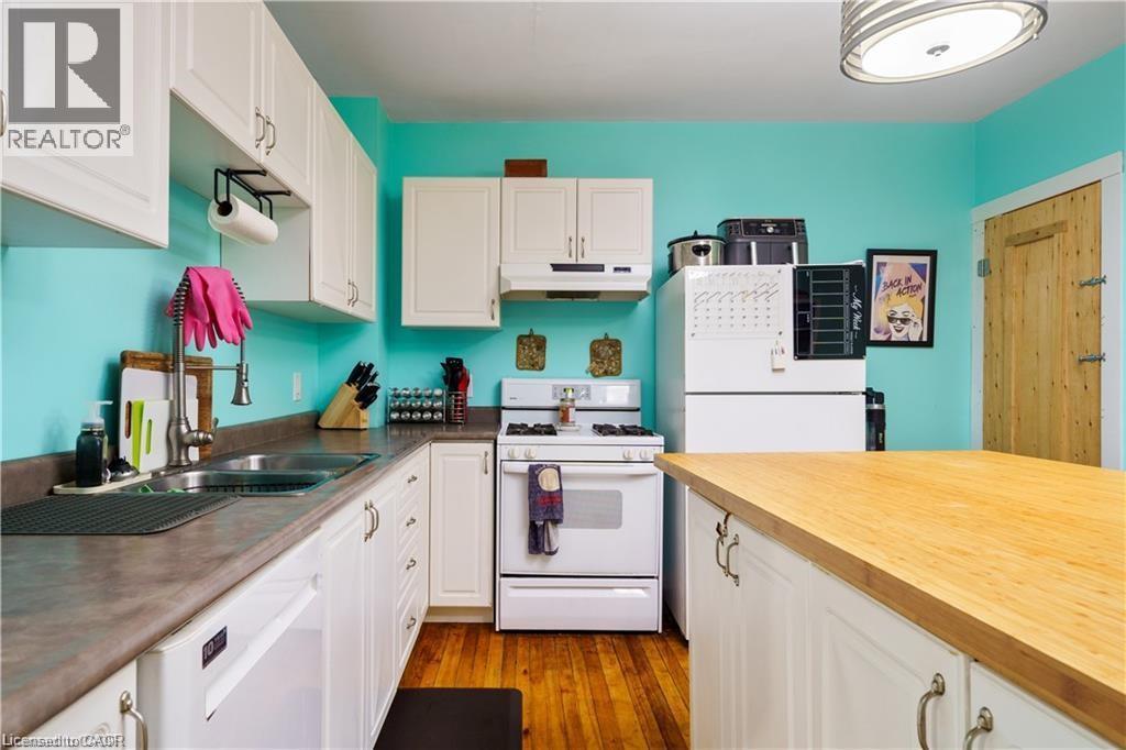 The kitchen features white cabinetry, a double basin sink, and a white refrigerator - 219 Avondale Street, Hamilton, ON - Indoor Photo Showing Kitchen With Double Sink