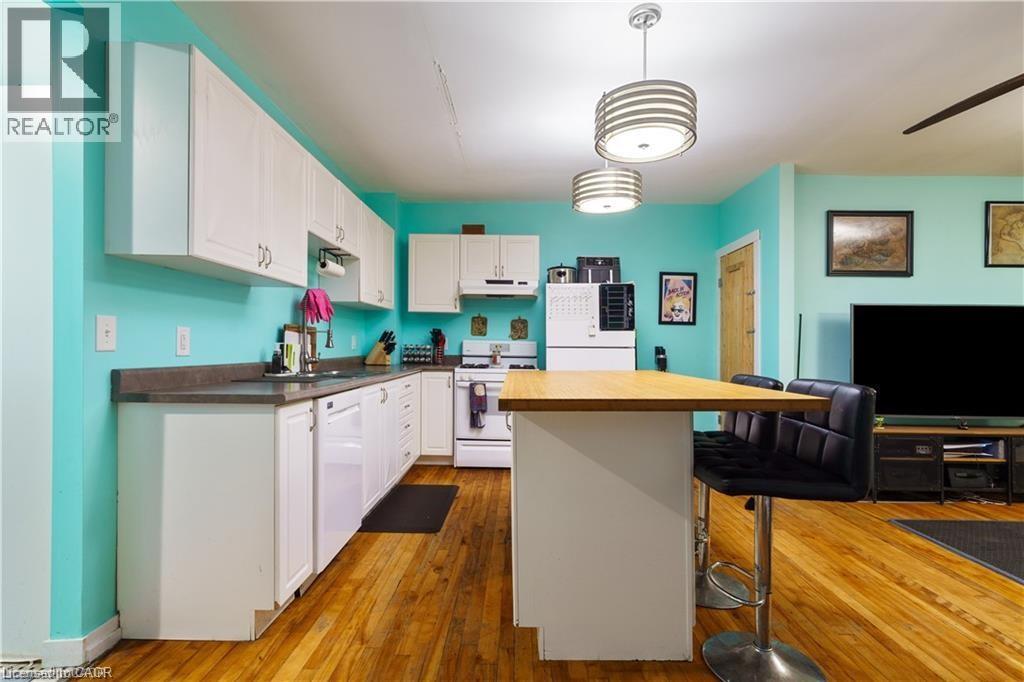 The kitchen features hardwood flooring, white cabinetry, and white appliances - 219 Avondale Street, Hamilton, ON - Indoor Photo Showing Kitchen