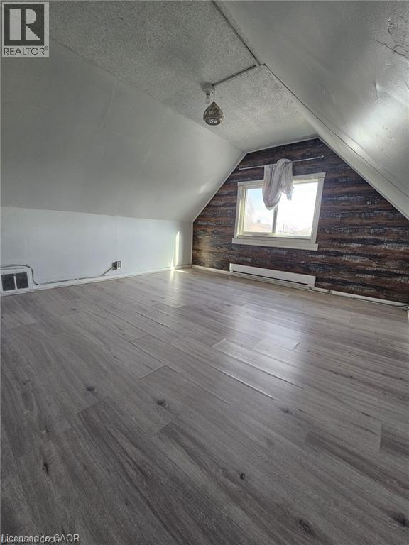 The property features an attic space with sloped ceilings, grey wood-look flooring, and a window providing natural light - 219 Avondale Street, Hamilton, ON - Indoor Photo Showing Other Room