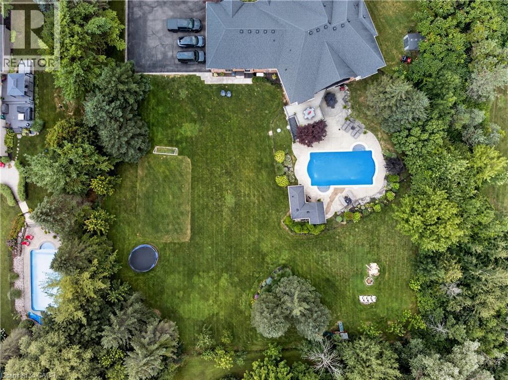 Expansive exterior grounds featuring a large in-ground swimming pool, stone patio, extensive green lawn, mature trees, and a separate asphalt driveway - 2050 15 Side Road, Milton, ON - Outdoor With In Ground Pool With View