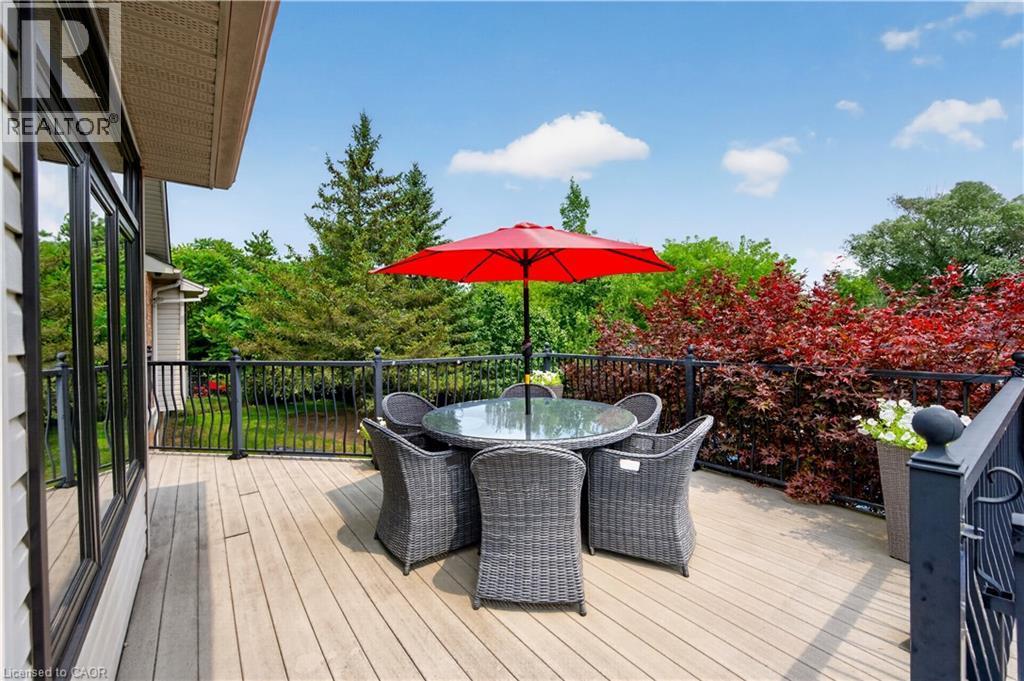 Expansive outdoor deck featuring wood-finish flooring, black metal railings, and vibrant surrounding foliage - 2050 15 Side Road, Milton, ON - Outdoor With Deck Patio Veranda With Exterior