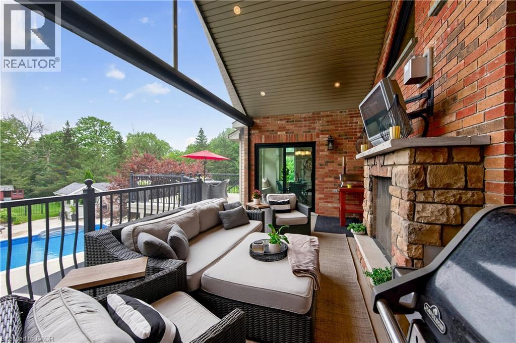 Expansive covered outdoor living space featuring a stone-clad fireplace with mantel, brick exterior wall, and integrated ceiling lighting - 2050 15 Side Road, Milton, ON - Outdoor With Exterior
