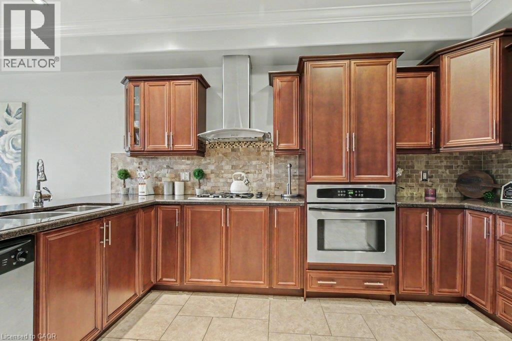 Kitchen featuring wood cabinetry, stainless steel appliances, a tile backsplash, and dark countertops - 284 Normanhurst Avenue, Hamilton, ON - Indoor Photo Showing Kitchen With Double Sink