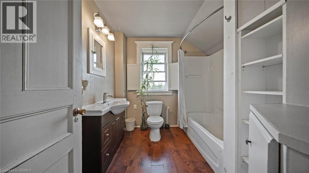 Bathroom featuring wood-finish flooring, a contemporary vanity with an integrated sink, a built-in tub and shower unit, and open shelving - 3211 Highway 3, Jarvis, ON - Indoor Photo Showing Bathroom