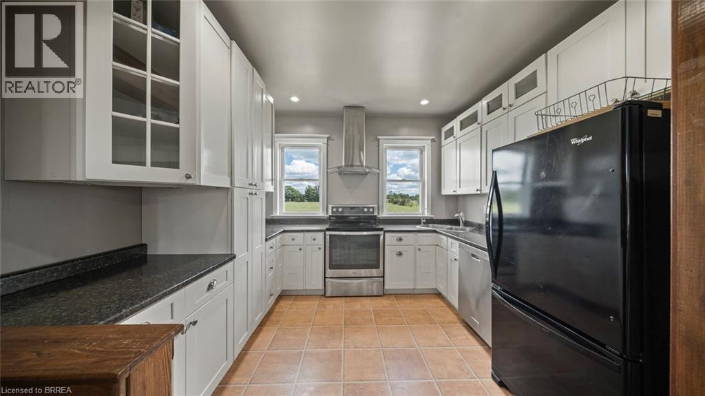 U-shaped kitchen featuring white cabinetry, dark countertops, stainless steel appliances, and terra cotta tile flooring - 3211 Highway 3, Jarvis, ON - Indoor Photo Showing Kitchen