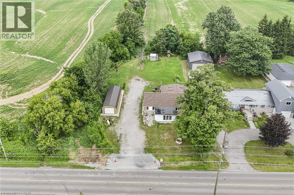 Expansive property featuring a single-story residence with a brown shingle roof, accompanied by two detached accessory buildings and a gravel driveway - 7332 Twenty Road E, Glanbrook, ON - Outdoor With View
