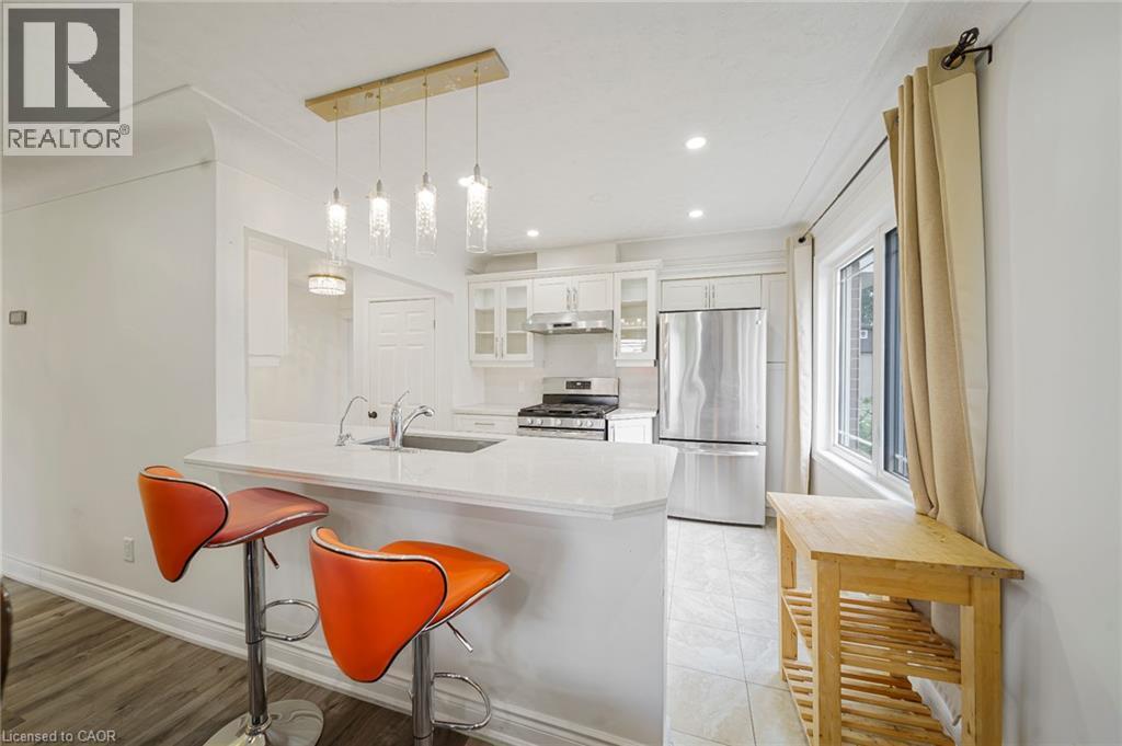 Kitchen featuring white cabinetry, stainless steel appliances, a peninsula with a light-toned countertop, a stainless steel sink with a gooseneck faucet, and recessed lighting - 7332 Twenty Road E, Glanbrook, ON - Indoor Photo Showing Kitchen With Upgraded Kitchen