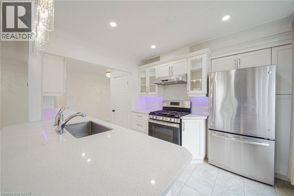 Kitchen featuring an undermount sink, a chrome pull-down faucet, a stainless steel gas range with coordinating vent hood, and a stainless steel refrigerator - 7332 Twenty Road E, Glanbrook, ON - Indoor Photo Showing Kitchen