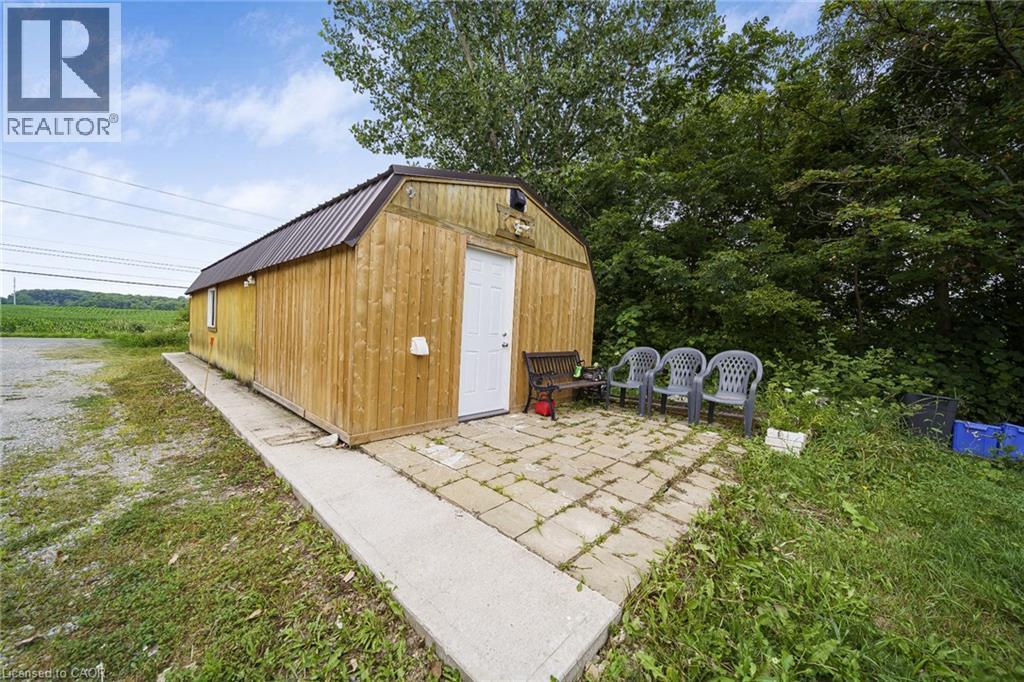 Wood-sided outbuilding featuring a brown metal roof, white entry door, and a single window - 7332 Twenty Road E, Glanbrook, ON - Outdoor