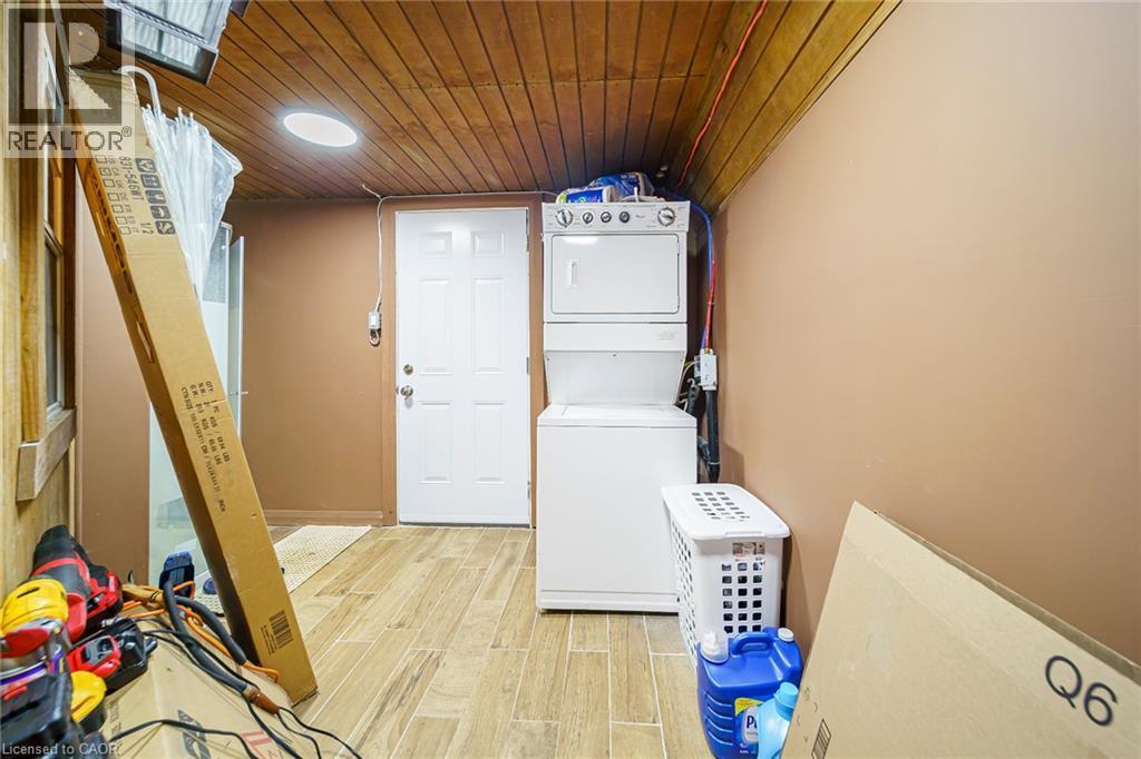 Utility area featuring wood-finish flooring, a wood plank ceiling, and a stacked washer and dryer unit - 7332 Twenty Road E, Glanbrook, ON - Indoor Photo Showing Laundry Room