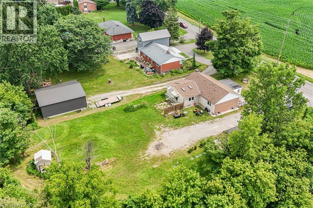 Expansive property featuring a main residence with a light-colored exterior and brown roof, a detached dark-paneled outbuilding with a metal roof, and a gravel driveway - 7332 Twenty Road E, Glanbrook, ON - Outdoor