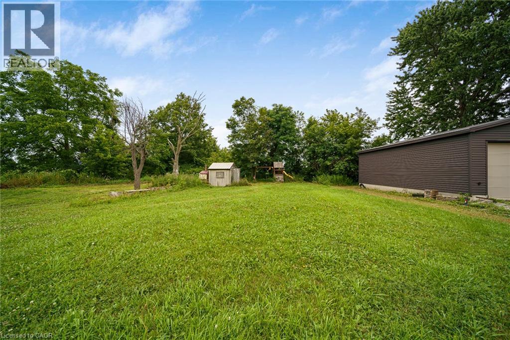 Expansive grass lawn featuring a detached accessory building, mature trees, a smaller storage shed, and a large outbuilding with a garage door - 7332 Twenty Road E, Glanbrook, ON - Outdoor