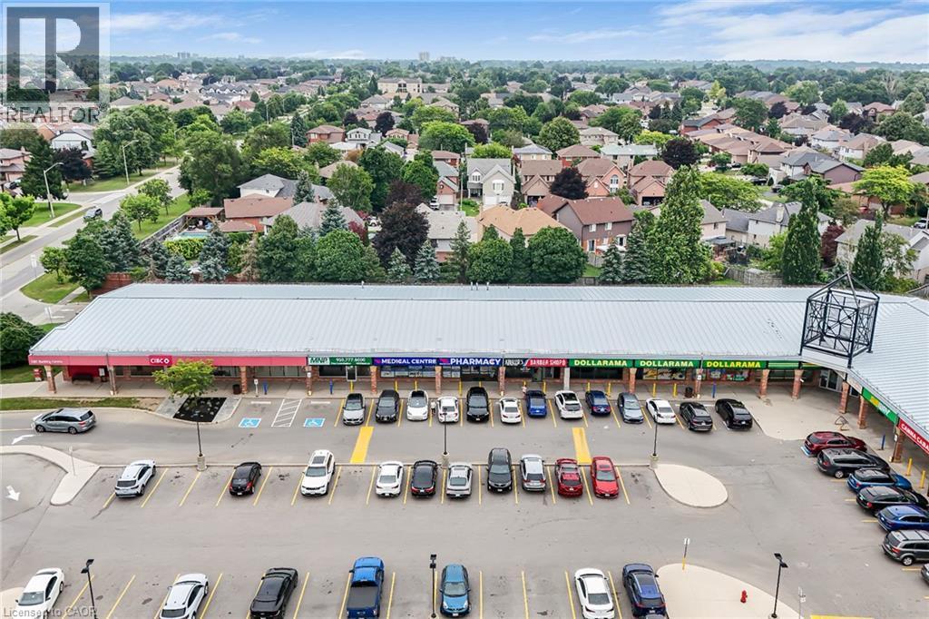 Retail plaza featuring multiple storefronts under a metal roof, a prominent parking lot, and surrounding residential areas - 7332 Twenty Road E, Glanbrook, ON - Outdoor With View