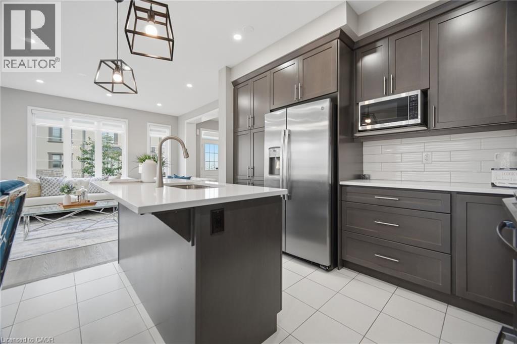 Spacious kitchen featuring an island with sink, dark cabinetry, stainless steel appliances, white subway tile backsplash, and light-toned tile flooring - 542 Boyd Lane, Milton, ON - Indoor Photo Showing Kitchen With Upgraded Kitchen