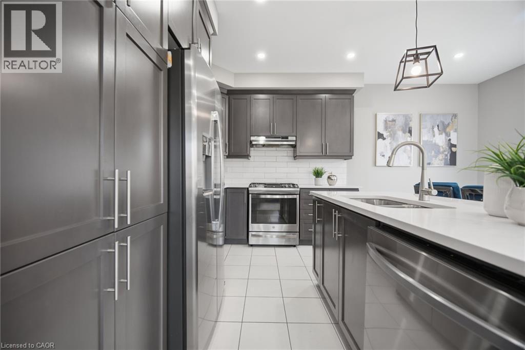 Modern kitchen featuring dark cabinetry, stainless steel appliances, white subway tile backsplash, and a large island with an undermount sink - 542 Boyd Lane, Milton, ON - Indoor Photo Showing Kitchen With Upgraded Kitchen