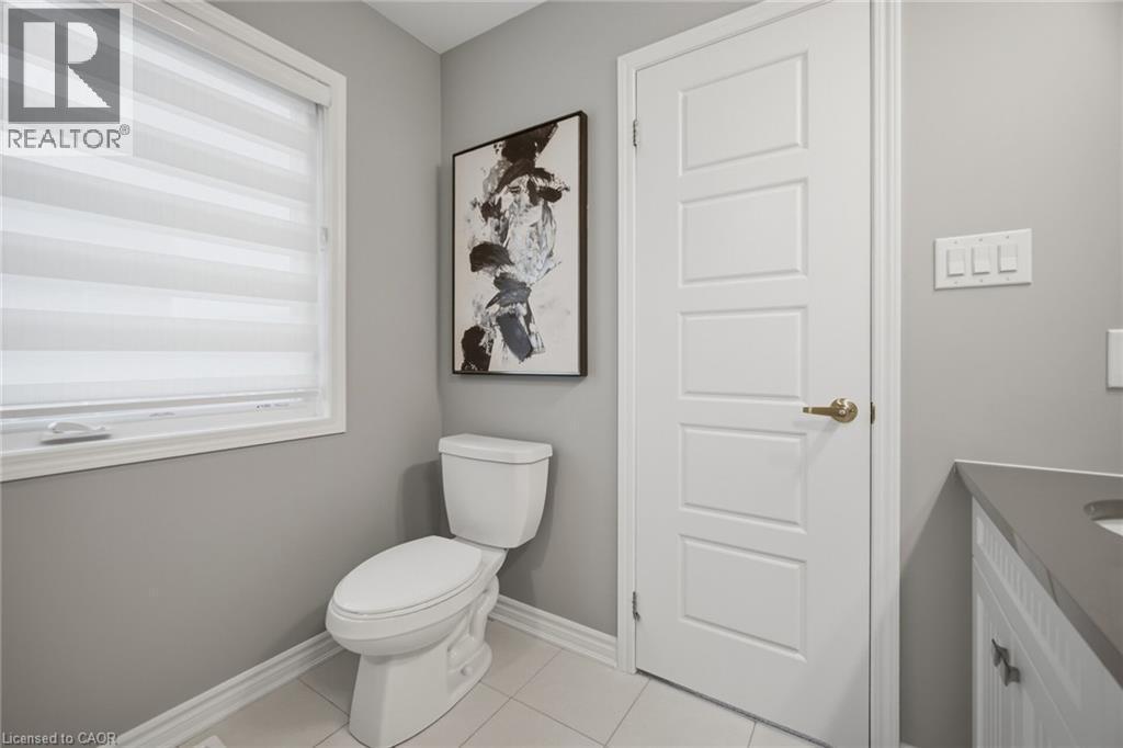Bathroom featuring a single window with blinds, a sleek white toilet, light gray walls, a four-panel interior door, and a built-in vanity with a gray countertop - 542 Boyd Lane, Milton, ON - Indoor Photo Showing Bathroom