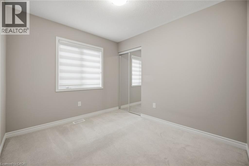 Neutral-toned interior room featuring light-colored carpet, a window with layered shades, and a mirrored sliding closet door - 542 Boyd Lane, Milton, ON - Indoor Photo Showing Other Room