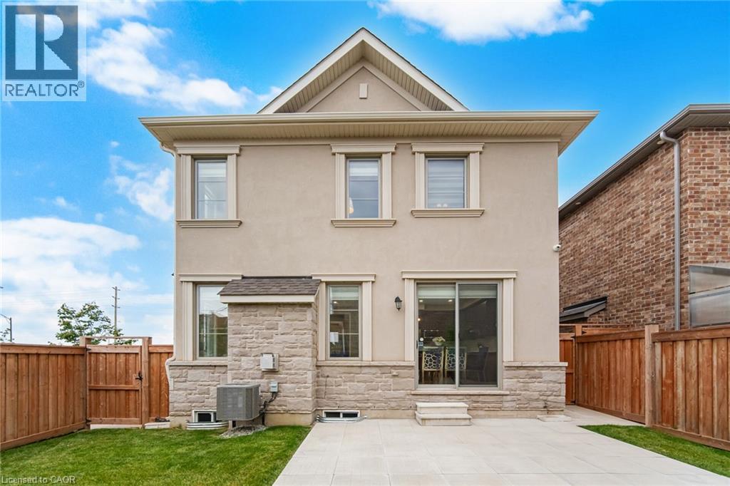 Rear exterior featuring stucco and stone veneer finishes, multiple windows, a sliding glass patio door, a concrete patio, and a grass lawn - 542 Boyd Lane, Milton, ON - Outdoor