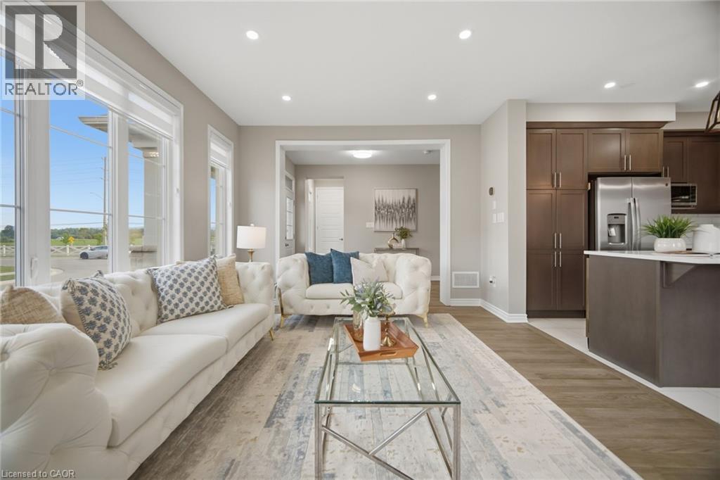 Open-concept living space featuring wood-finish flooring, a kitchen island with white countertop, dark wood-finish cabinetry, stainless steel refrigerator, and recessed lighting - 542 Boyd Lane, Milton, ON - Indoor Photo Showing Living Room
