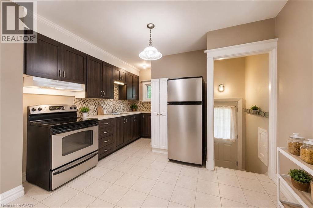 Kitchen featuring dark wood-finish cabinetry, stainless steel appliances, a mosaic tile backsplash, and light-toned tile flooring - 74 Royal Avenue, Hamilton, ON - Indoor Photo Showing Kitchen