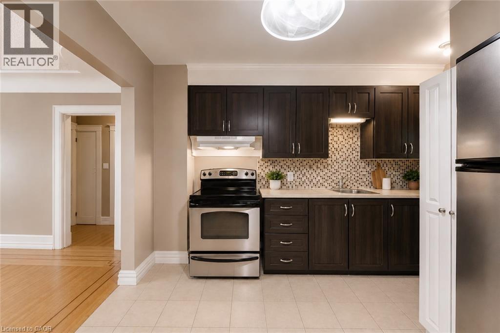 Kitchen featuring dark wood-finish cabinetry, stainless steel appliances, mosaic tile backsplash, and light-toned countertop - 74 Royal Avenue, Hamilton, ON - Indoor Photo Showing Kitchen