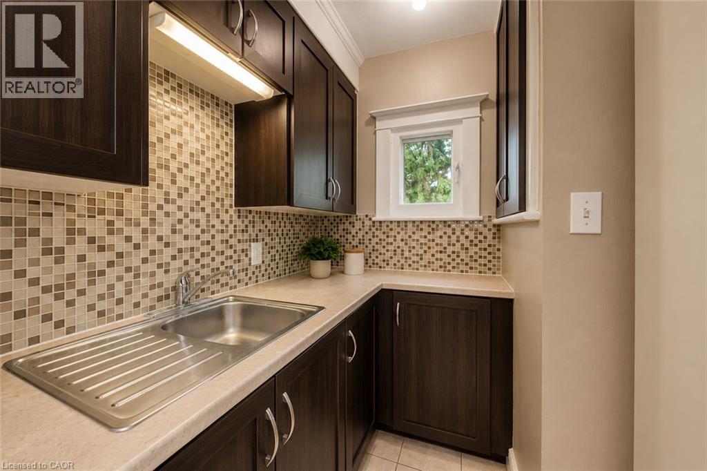 Kitchen area featuring dark wood-finish cabinetry, a mosaic tile backsplash, and light-toned countertops - 74 Royal Avenue, Hamilton, ON - Indoor Photo Showing Kitchen