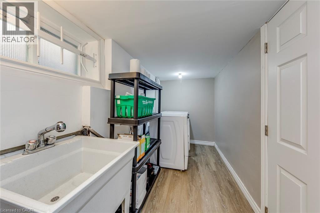 Laundry area featuring a utility sink with a pull-out spray faucet, wood-finish flooring, a white paneled door, and a frosted glass window - 74 Royal Avenue, Hamilton, ON - Indoor Photo Showing Laundry Room