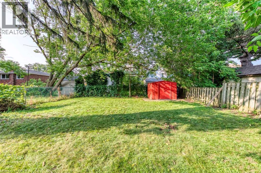 Expansive grassy yard area featuring mature trees providing natural canopy, a red storage shed, chain-link fencing, and a wood privacy fence - 74 Royal Avenue, Hamilton, ON - Outdoor