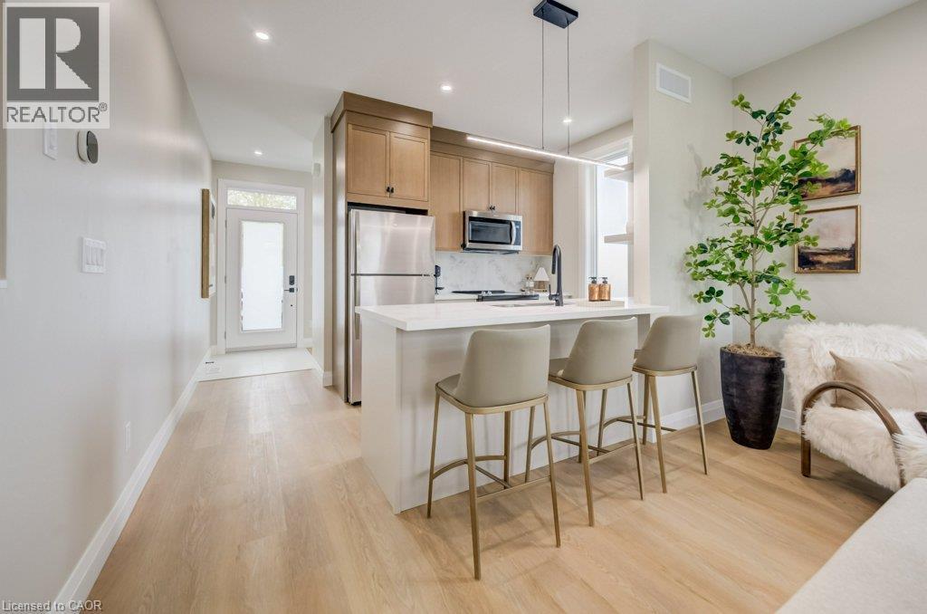 Open-concept kitchen featuring light wood-finish flooring, a white island with an integrated sink, stainless steel appliances, and wood cabinetry - 210 Heritage Drive Unit# Main, Kitchener, ON - Indoor Photo Showing Kitchen With Upgraded Kitchen