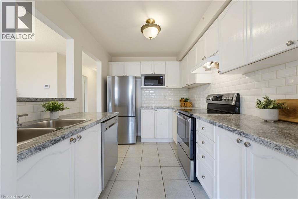 Well-appointed kitchen featuring white cabinetry, subway tile backsplash, stainless steel appliances, granite-style countertops, and tile flooring - 4425 Peter Drive, Burlington, ON - Indoor Photo Showing Kitchen With Double Sink With Upgraded Kitchen