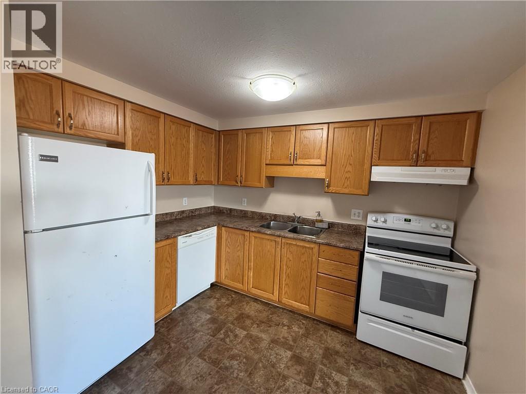 Kitchen featuring light wood cabinetry, white appliances, laminate countertops, a double basin sink, and sheet vinyl flooring - 11 Hackberry Street Unit# 1, Kitchener, ON - Indoor Photo Showing Kitchen With Double Sink