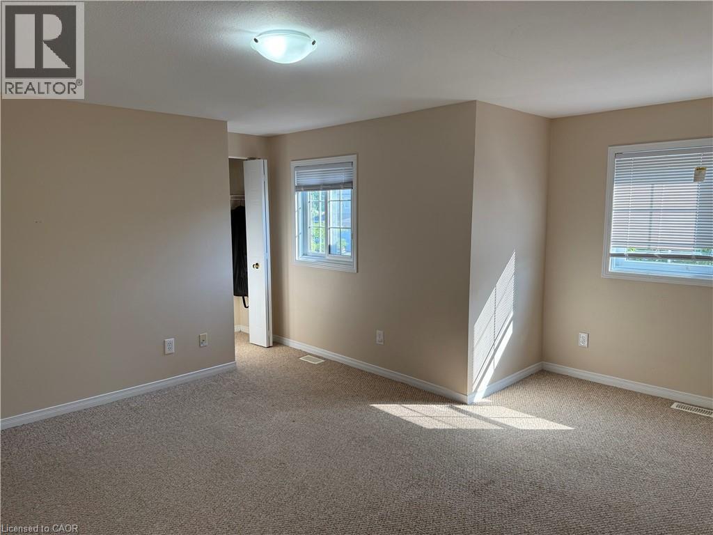 Neutral-toned room featuring two windows, light beige carpeting, white trim, and a semi-flush mount ceiling light - 11 Hackberry Street Unit# 1, Kitchener, ON - Indoor Photo Showing Other Room