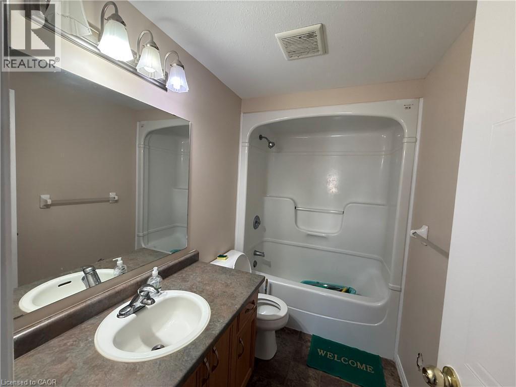 Bathroom featuring a single vanity with an integrated sink, a large wall-mounted mirror, and a combination shower-tub unit - 11 Hackberry Street Unit# 1, Kitchener, ON - Indoor Photo Showing Bathroom