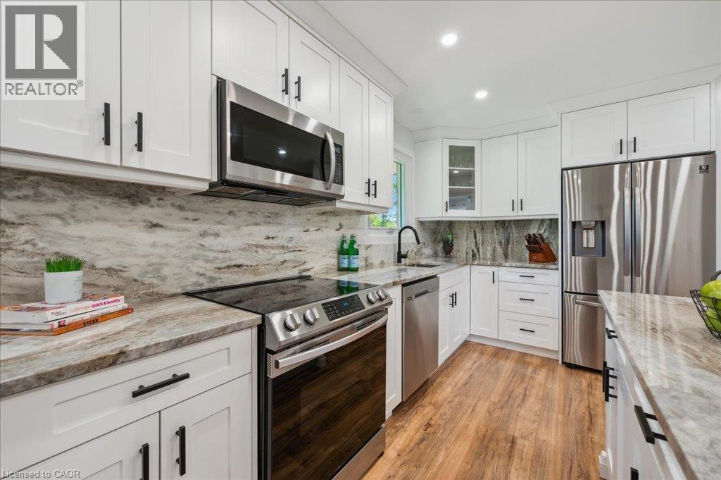 Kitchen featuring white shaker-style cabinetry, stainless steel appliances, marbled countertops, a matching full-height backsplash, and wood-finish flooring - 76 Lower Canada Crescent, Kitchener, ON - Indoor Photo Showing Kitchen With Upgraded Kitchen