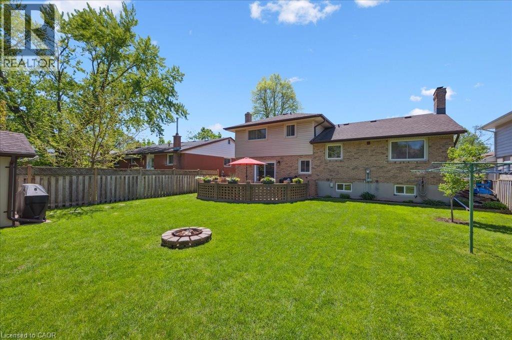Expansive rear lawn featuring a stone-ringed fire pit, a private wood fence perimeter, and mature trees - 76 Lower Canada Crescent, Kitchener, ON - Outdoor With Backyard
