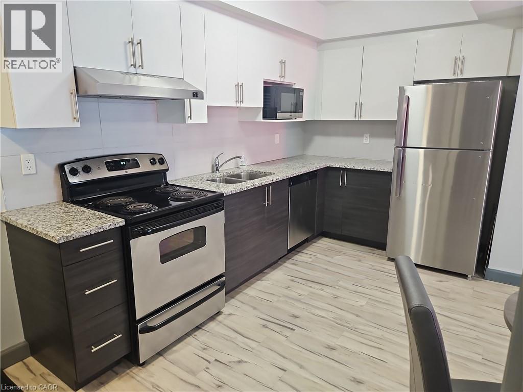 Kitchen featuring stainless steel appliances, under cabinet range hood, light wood-type flooring, white cabinets, and light stone counters - 258B Sunview Street Unit# 255, Waterloo, ON - Indoor Photo Showing Kitchen With Stainless Steel Kitchen With Double Sink