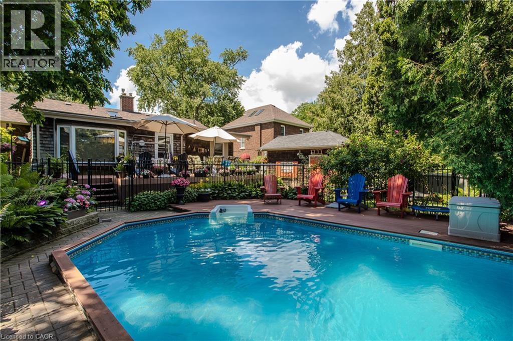 In-ground swimming pool with a surrounding dark wood-finish deck and brick paver accents - 569 Locust Street, Burlington, ON - Outdoor With In Ground Pool With Deck Patio Veranda With Backyard