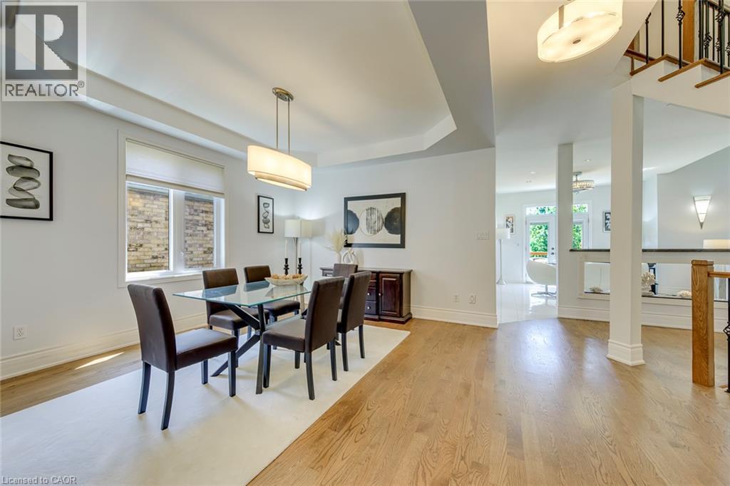 Open-concept dining area featuring hardwood flooring, a contemporary linear chandelier, and tray ceiling detail - 2380 Woodcrest Drive, Oakville, ON - Indoor Photo Showing Dining Room