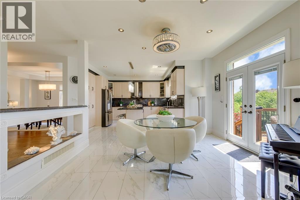 Bright eat-in kitchen area featuring white marble-look tile flooring, a contemporary ceiling fixture, recessed lighting, and double glass-paneled doors with transom windows - 2380 Woodcrest Drive, Oakville, ON - Indoor Photo Showing Other Room With Fireplace