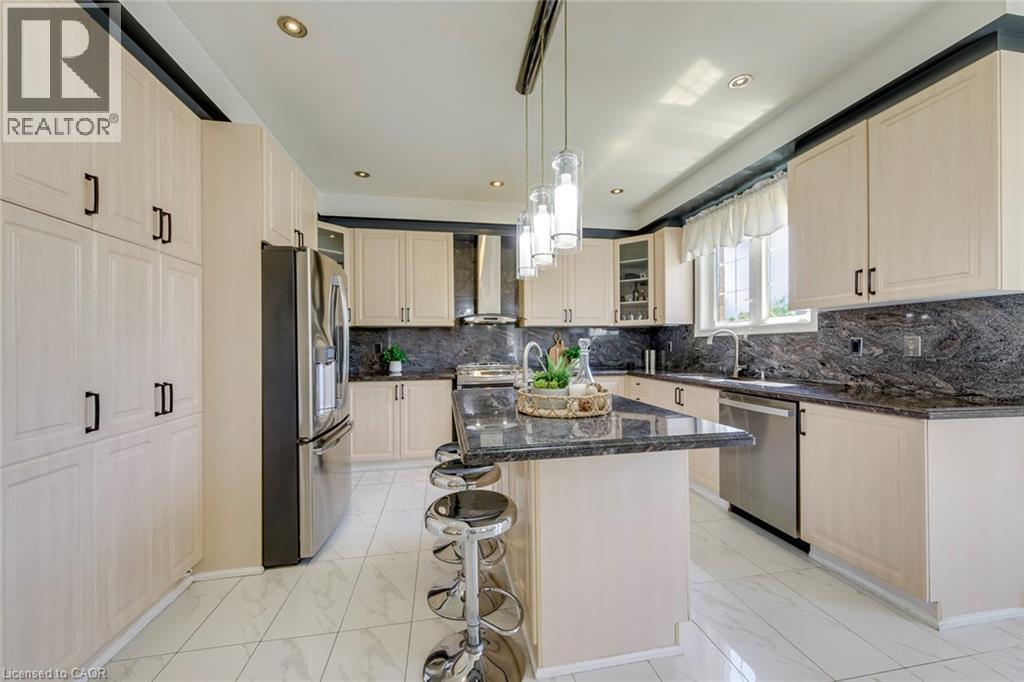 Contemporary kitchen featuring a central island with counter seating, light wood-finish cabinetry, dark stone countertops, stainless steel appliances, and recessed lighting - 2380 Woodcrest Drive, Oakville, ON - Indoor Photo Showing Kitchen With Upgraded Kitchen