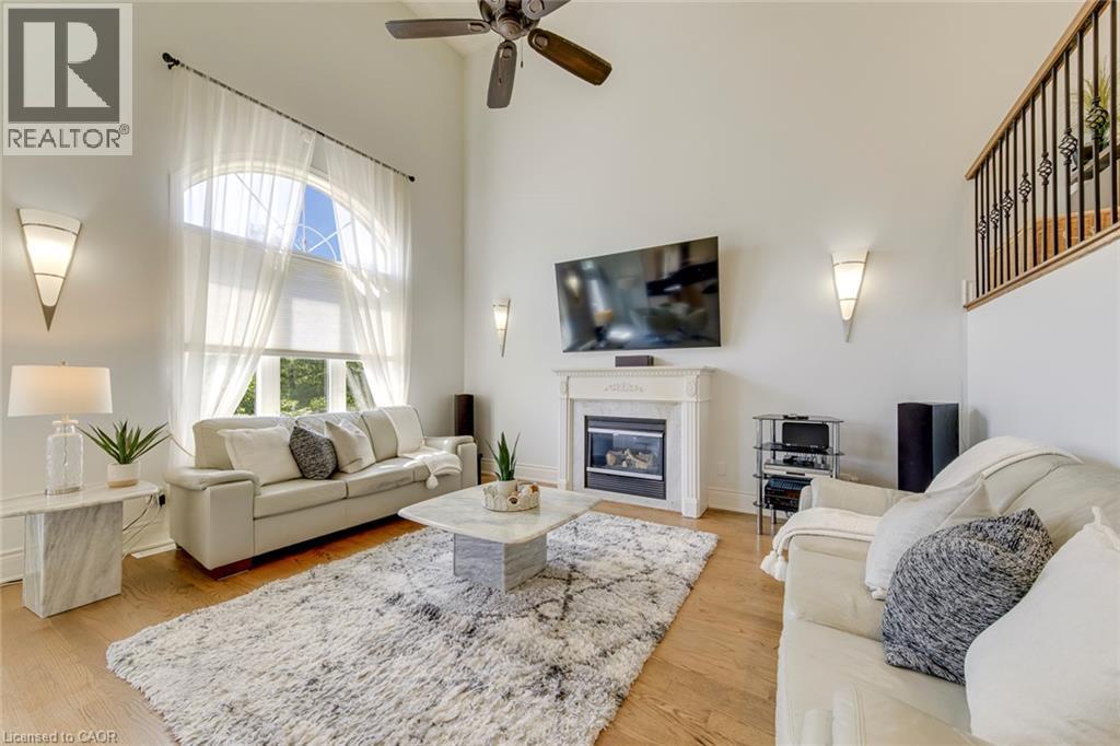 Two-story living area featuring a large arched window with sheer drapes, a ceiling fan, and hardwood flooring - 2380 Woodcrest Drive, Oakville, ON - Indoor Photo Showing Living Room With Fireplace