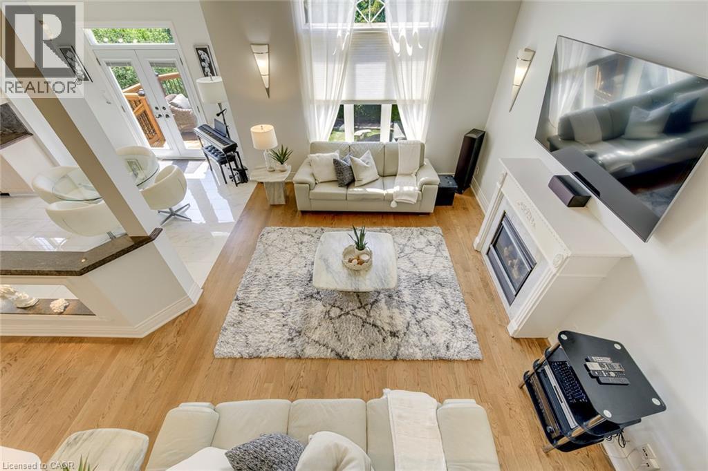 Two-story living area with hardwood flooring, a white mantel fireplace, and high windows featuring sheer drapery - 2380 Woodcrest Drive, Oakville, ON - Indoor