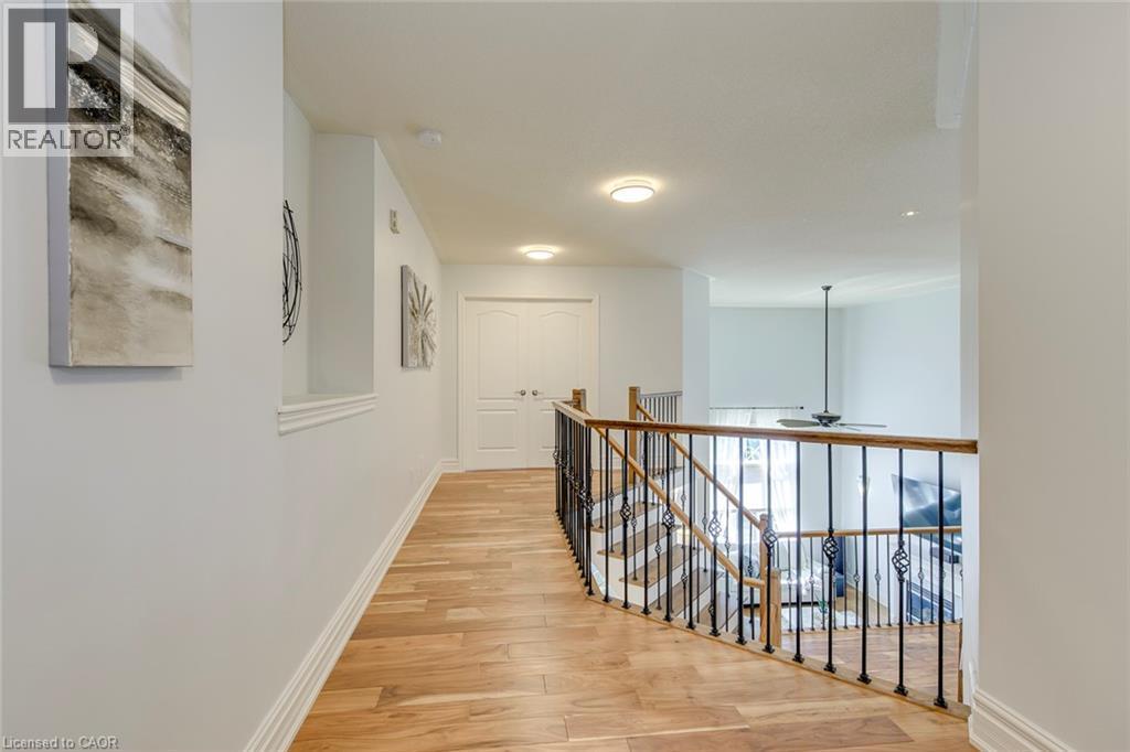 Upper-level hallway featuring wood-finish flooring, white baseboards, and a railing with dark metal spindles and a wood-finish top rail - 2380 Woodcrest Drive, Oakville, ON - Indoor Photo Showing Other Room